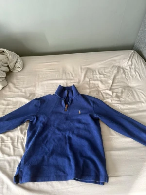 Blå halvzip tröja från Polo Ralph Lauren - Snygg blå stickad tröja från Polo Ralph Lauren med halvzip och klassisk broderad logga på bröstet. Tröjan har långa ärmar och hög krage, perfekt för lager på lager. Passar dig som gillar stilrena och tidlösa plagg.