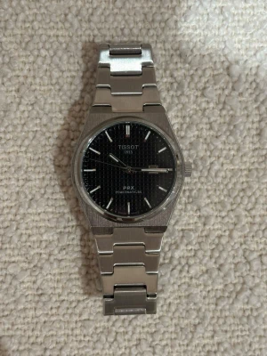 Tissot PRX - Snygg Tissot PRX Powermatic 80 klocka med svart urtavla och stilren länk i silverfärgat stål. Klassisk rund form och tydliga indexmarkeringar. Perfekt accessoar för dig som gillar tidlös design och kvalitet.