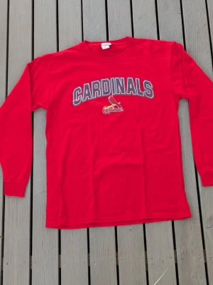Röd Cardinals långärmad t-shirt - Snygg röd långärmad t-shirt med Cardinals-tryck och logga på bröstet. Perfekt för dig som gillar sportig stil och vill sticka ut lite extra. Rund halsringning och mjukt material som känns skönt mot huden.