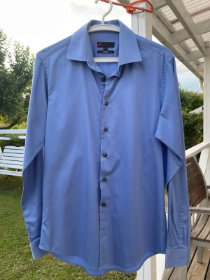 Ljusblå Dressmann slim fit skjorta strl M - Ljusblå Dressmann-skjorta i slim fit, storlek M / 39-40. 98% bomull och 2% elastan. Klassisk modell med mörka knappar. Mycket bra skick och använd endast ett fåtal gånger. Säljes eftersom den inte används längre. Nypris: 399kr