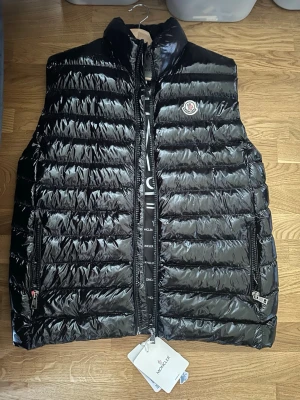 Svart dunväst från Moncler - Snygg svart dunväst från Moncler. Storlek 4 men sitter som M. Aldrig använd. Köpt för 4500 för några år sen men kom aldrig till användning säljer för 599kr. Vid intresse eller fler bilder hör av er!!