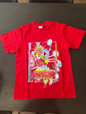 Röd Supreme t-shirt med tryck - Supreme t-shirt i rött med färgstarkt grafiskt tryck framtill som visar en tecknad figur och text. Klassisk passform och rund hals. Tillverkad i 100% bomull för skön känsla. Perfekt för dig som vill sticka ut med streetwear-vibe.