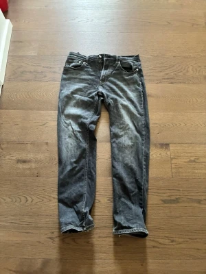 Grå slitna raka jeans - Ett par grå jeans med rak passform och slitna detaljer. Jeansen har klassisk femficksdesign och knappgylf. Materialet är denim i bomull och färgen har en tvättad look med ljusare partier. Perfekta för en avslappnad och trendig stil.