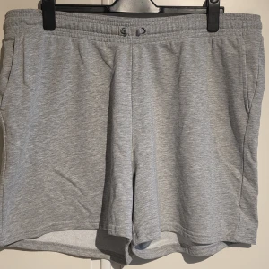 Grå mjuka shorts med snörning - Ett par ljusgrå shorts i mjukt material med elastisk midja och snörning framtill. Shortsen har en avslappnad passform och sidofickor, perfekta för chill dagar eller träning.