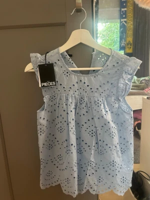 Ljusblå broderad topp  - Säljer en supersöt ljusblå topp med broderade hålmönster och volangdetaljer vid axlarna, nyskick med lappen kvar då den aldrig kommit till användning, köpt för 349kr💕