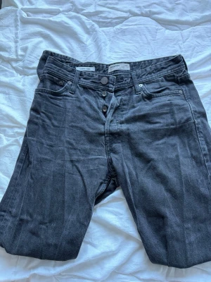 Svarta jeans från Jack & Jones 28/32 - Snygga svarta jeans från Jack & Jones med klassisk femficksdesign och knäppning med knappar. Jeansen har en rak passform och är tillverkade i bomull. Perfekta för en stilren och avslappnad look.