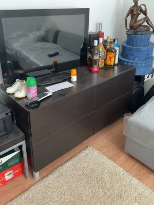 Svart TV-bänk med förvaring - Modern svart TV-bänk i trä med två stora lådor och silverfärgade ben. Perfekt för att ställa TV och förvara elektronik eller andra prylar. Stilren och enkel design som passar i de flesta rum.
