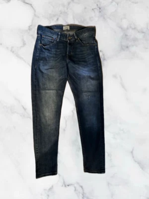 Mörkblåa Jack & Jones jeans - Snygga mörkblå slim fit jeans med klassisk femficksdesign och lätt slitna detaljer framtill. Jeansen har normal midja, dragkedja och knappstängning samt kontrastsömmar. Perfekta för en trendig och avslappnad stil. W30 L31