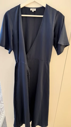 Omlottklänning med kort ärm - Elegants och smickrande midi-klänning i omlottmodell från Bubbleroom Occasion. Klänningen har v-ringning, korta ärmar och ett fint fall i glänsande satinmaterial. Passar perfekt till fest, bröllop eller middagar.