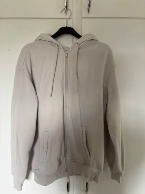 Beige ziphoodie  - Säljer en beige hoodie med dragkedja framtill och två fickor. Hoodien har justerbar huva med snören och ribbade muddar vid ärmar och nederkant. Perfekt för en avslappnad och stilren look. Bra skick