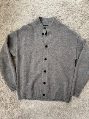 Grå yllekofta från Massimo Dutti - Grå kofta med svarta knappar i kanonskick. Koftan har en högre krage och är i ett mjukt o härligt material. Perfekt nu när hösten stundar🍂 storlek S