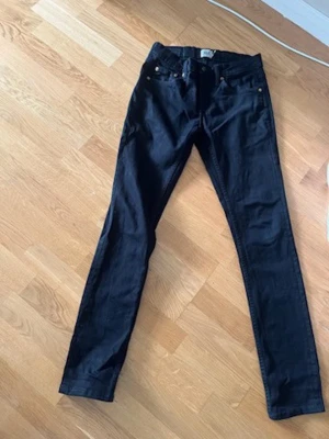 Nyskick Svarta skinny jeans med koppardetaljer - Snygga svarta skinny jeans med klassisk femficksdesign och kopparfärgade nitar. Jeansen har bälteshällor och knappstängning framtill. Perfekta för dig som gillar en slimmad passform och stilren look.