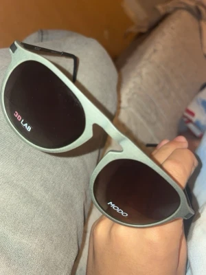 Gråa solglasögon från Modo - Snygga solglasögon från Modo med grå bågar och mörka glas. De har en klassisk rundad form som passar till de flesta stilar. Perfekta för att ge din look en cool touch i solen. Pris kan diskuteras 