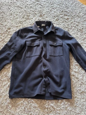 Mörkblå overshirt från Selected Homme - Stilren mörkblå overshirt från Selected Homme med två bröstfickor med lock och knappar. Klassisk krage. Säljer denna eftersom den har växt ut på mig väldigt fin Overshirt med väldigt skön och bra material tveka inte o höra av dig vid funderingar 💪💪