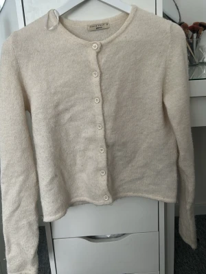 Beige kofta från Gina Tricot - Mysig beige kofta från Gina Tricot i mjukt stickat material. Koftan har rund halsringning, långa ärmar och knäpps med vita knappar framtill. Enkel och stilren design som passar till det mesta.
