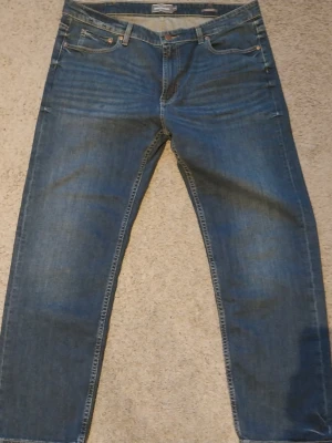 Blå jeans från Dressmann - Klassiska blå jeans från Dressmann med raka ben och fem fickor. Jeansen har en snygg tvättad look och kontrastsömmar. Perfekta för en avslappnad stil och tillverkade i slitstarkt denimtyg.