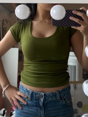 Olivgrön croppad t-shirt - Snygg olivgrön croppad t-shirt med rund halsringning och korta ärmar. Perfekt till ett par jeans för en avslappnad och trendig look. Materialet känns mjukt och stretchigt. Köpte på loppis står inget märke! 