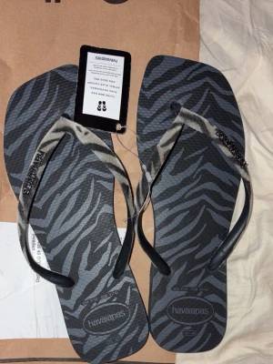 Zebramönstrade flip-flops Havaianas - Snygga flip-flops från Havaianas med zebramönster i svart och grått. Oanvända med lappen kvar. Köpte från sellpy för 330kr men passade inte. 