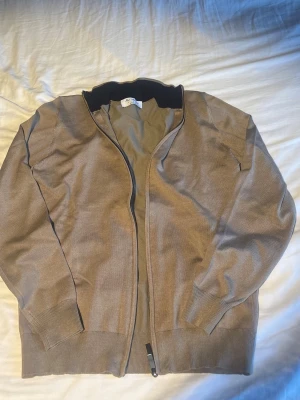 Beige ziptröja av preium kashmir och merinoull - En stilren grå ziptröja från Max Martini från Milano, med ståkrage och långa ärmar. Tröjan har ribbade muddar vid ärmslut och nederkant samt dragkedja framtill. Tillverkad i ett tunt, mjukt premium kashmir och merinoulls material som passar perfekt till lager på lager. (Har storlek L men är något liten i storleken). Nytt skick, aldrig använts.