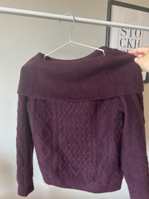 Vinröd off shoulder stickad tröja - Vinröd stickad tröja från H&M Divided med bred off shoulder-krage och diskret mönsterstickning framtill. Tröjan har långa ärmar och ribbade muddar. Perfekt för dig som vill ha en trendig och mysig look i höst och vinter. Den är oanvänd då den var lite för liten för mig och jag inte han lämna tillbaka i tid💕