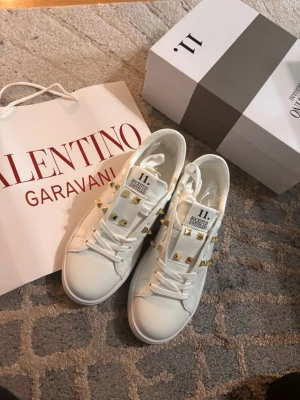 Vita Valentino sneakers med guld nitar  - Säljer ett par vita Valentino  med guldiga nitar längs sidorna och på plösen. Storlek 30 men passar även om man har 38