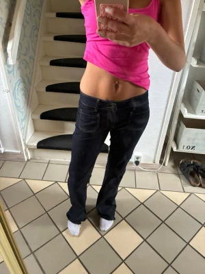 Mörkblå bootcut jeans med kontrastsömmar - Säljer ett par mörkblå bootcut jeans med snygga kontrastsömmar och klassisk femficksdesign. Jeansen har låg midja och utsvängda ben, perfekta för en avslappnad och trendig look. Materialet är kraftigt denim som ger en schysst passform.