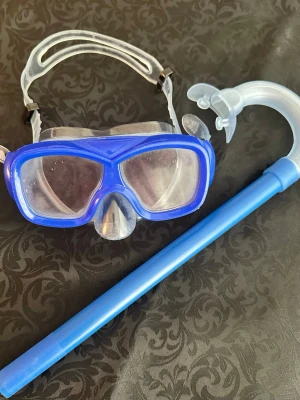 Blå snorkelset med cyklop barn 7-11 år  - Säljer ett snorkelset med blå cyklop och matchande snorkel. Masken har genomskinlig silikonram och justerbart band för bekväm passform. Perfekt för strandhäng och snorkling. Materialet är plast och silikon.