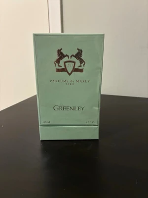 Parfums de Marly Greenley 125ml - Greenley från Parfums de Marly är en exklusiv parfym i en stilren, ljusgrön kartong med elegant logotyp och text i silver. Doften är Eau de Parfum och förpackningen utstrålar lyx och modernitet. Perfekt för dig som gillar unika och fräscha dofter.