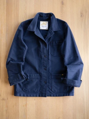 Navy Chore Jacket från Le Mont St Michel - Klassisk mörkblå overshirt från Le Mont St Michel i robust bomullstyg. Modellen har tre utanpåliggande fickor, knäppning framtill med svarta knappar och en avslappnad krage. Perfekt lager-på-lager-plagg för en stilren look.