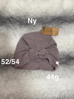 Ljuslila stickad mössa med rosett - Supersöt ljuslila stickad mössa från Newbie med en dekorativ rosett framtill. Mössan är mjuk och har en fin strukturstickning som ger en mysig känsla. Perfekt accessoar för att hålla värmen och samtidigt se stylish ut.🌸 Ny med tagg. Storlek 52/54