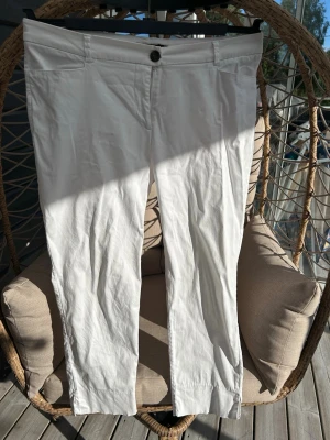 Capri jeans strl. 44 - Vita capri jeans från Seppälä Woman i rak modell. Byxorna har knappgylf, två framfickor och är gjorda i ett mjukt bomullsmaterial med lite stretch. Slit längst ner på båda benen på utsidan