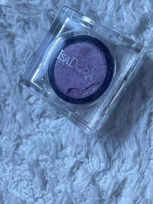 Lila ögonskugga från IsaDora - En snygg lila ögonskugga från IsaDora i en rund dosa med transparent lock. Färgen är skimrande och passar perfekt för att skapa kreativa och färgstarka ögonmakeuper. Förpackningen är smidig att ta med i väskan.