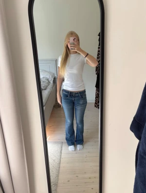 Blå bootcut jeans med låg midja - Säljer ett par blå bootcut jeans med låg midja och klassiska fickor både fram och bak. Jeansen har en snygg tvätt och är i ett stretchigt denimtyg som sitter bekvämt. Jeansen är i storlek 0 men passar mig som i vanliga fall har storlek S.