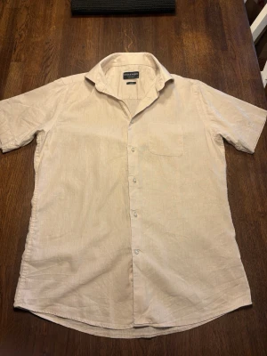 Beige linneskjorta med kort ärm - Snygg beige skjorta från Bruun & Stengade i linne med korta ärmar och klassisk krage. Perfekt för varma dagar och enkel att matcha med olika outfits. Hör av er om ni har några frågor eller om ni vill ha fler bilder! 