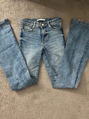 Blå low waist jeans från Zara  - Säljer ett par klassiska blå jeans från Zara med bootcut passform och low waist. Jeansen har en snygg tvättad look och silverfärgad knapp. Perfekta till en avslappnad stil och passar till det mesta i garderoben.