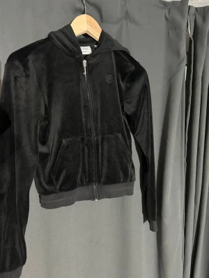Svart juicy couture ziptröja  - Mjuk och skön svart hoodie i velour med dragkedja framtill och fickor. Tröjan har huva och ribbade muddar vid ärmslut och nederkant. Perfekt för en avslappnad och trendig look. Den är i storlek 12-13 år💞