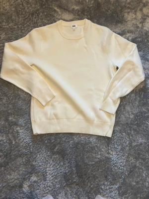 Vit rundhalsad tröja Uniqlo - Klassisk vit tröja från Uniqlo med rund halsringning och långa ärmar. Tillverkad i ett mjukt och tunt material som passar perfekt för lager på lager. Enkel och stilren design utan mönster eller tryck.