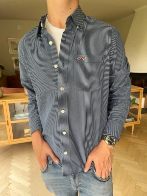 Hollister skjorta randig herr blå vintage  - Fin långärmad skjorta från Hollister i mörkblått och vitrandigt mönster. Klassisk modell med logga på bröstfickan. Perfekt till både vardag och fest. Storlek S. Mycket gott skick!#hollister #skjorta #randig #herrkläder #långärmad #mode #vinted #casual. Passar dig som är 173-186cm