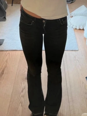 Svarta bootcut jeans med låg midja - Säljer ett par svarta bootcut jeans med låg midja och klassiska fem fickor. Jeansen har utsvängda ben och sitter tight upptill. Perfekta för dig som gillar en trendig och avslappnad stil.