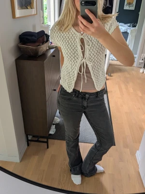 Vit stickad kofta - Säljer en vit, kortärmad kofta i stickat material med snygg snörning framtill. Toppen har ett öppet mönster och croppad passform som ger en trendig look. Perfekt att styla över ett linne eller topp för en cool layering-effekt.