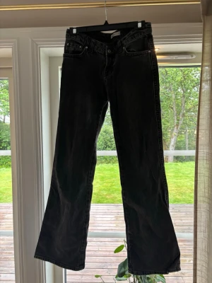 Svarta bootcut jeans med medel midja - Säljer ett par svarta bootcut jeans med medel midja och klassiska fem fickor. Jeansen har en lätt utsvängd passform nedtill och är tillverkade i denim. Perfekta för dig som gillar en avslappnad men trendig look.
