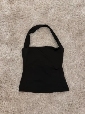 Halterneck topp - Snygg svart topp med breda band som går runt nacken. Enkel och stilren design - aldrig använd 