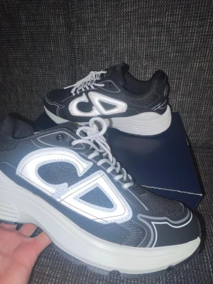 Svarta  sneakers med vit detalj - Snygga svarta sneakers  med stora vita detaljer på sidan och vita snören. Skorna har en chunky sula i vitt och svart samt mesh- och läderpaneler för en modern look. Perfekta för dig som vill sticka ut med exklusiva och trendiga sneakers.