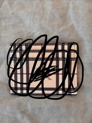 Bb plånbok  - Snyggt kortfodral i beige med klassiskt rutigt mönster i svart, vitt och rött. Fodralet har flera kortfack och är tillverkat i ett slätt material som ger en stilren look. Perfekt för dig som vill ha koll på dina kort med stil.