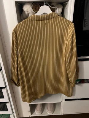 Randig beige kavaj från Part Two - Snygg beige kavaj med vita vertikala ränder från Part Two. Oversized passform med klassisk krage och slag, samt två fickor framtill. Tillverkad i ett mjukt och lätt material som ger en avslappnad look. Perfekt för att lyfta vilken outfit som helst.