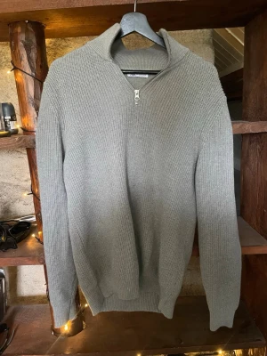 Grå stickad halvzip-tröja från Zara - Snygg grå stickad tröja från Zara med halvzip och hög krage. Tröjan har lång ärm och ribbade muddar vid ärmslut och nederkant. Perfekt för lager på lager och enkel att matcha med olika outfits.