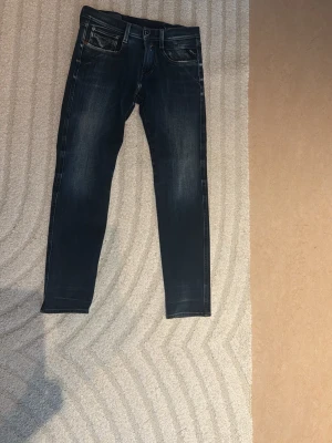 Mörkblå slim fit jeans med slitningar - Säljer ett par mörkblå slim fit jeans med snygga slitningar och tvättade detaljer. Jeansen har klassisk femficksdesign och kontrastsömmar. Materialet är denim i bomull med lite stretch för skön passform. Perfekta till en avslappnad stil.