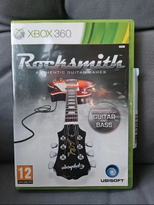 Rocksmith till Xbox 360 - Rocksmith är ett musikspel till Xbox 360 där du kan koppla in en riktig gitarr eller bas och spela över 50 klassiska och moderna rocklåtar. Omslaget visar en Epiphone Les Paul och spelet har stöd för multiplayer och olika svårighetsgrader.