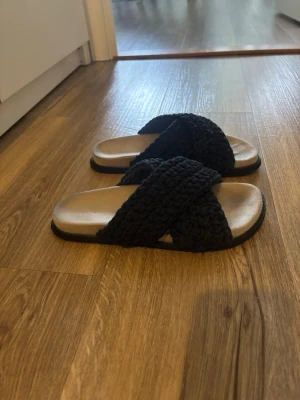 Svarta sandaler med flätade band - Säljer ett par svarta sandaler med breda, korslagda flätade band i textil. Sulan är beige och har en lätt upphöjd kant. Pris kan diskuteras.