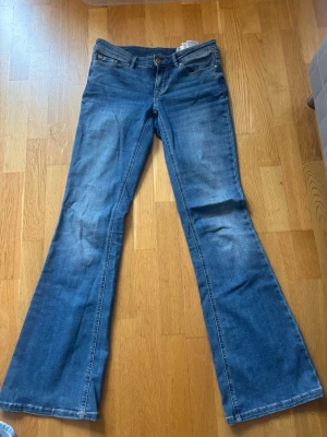 Blå bootcut jeans med låg midja - Säljer ett par klassiska blå bootcut jeans med låg midja och fem fickor. Jeansen har en snygg tvätt och lätt utsvängda ben. Perfekta till sneakers eller boots och ger en avslappnad men trendig look.